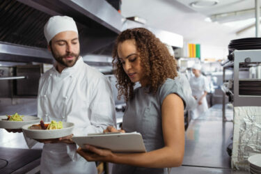 Chefs,Discussing,Menu,On,Clipboard,In,Commercial,Kitchen